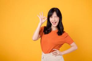 Young asian woman 30s wearing orange shirt showing okay sign gesture isolated on yellow background. Female person with hands gesture concept. photo
