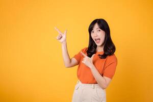 Spread happiness with a young Asian woman in her 30s, donning an orange shirt, pointing to free copy space on yellow background. recommending product concept. photo