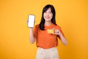 alegre asiático mujer en su 30, utilizando teléfono inteligente y crédito tarjeta en amarillo antecedentes. simplificado en línea pago compras. foto