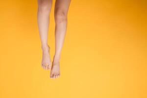 smooth and soft touch with a 30s person's close up legs against vibrant yellow background. Gentle and velvety foot concept. photo