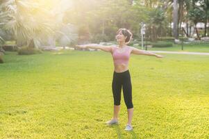 hembra persona que practica jogging. ajuste 30s joven asiático mujer en rosado ropa de deporte preparando calentar arriba cuerpo en parque antes de correr. sano al aire libre estilo de vida con aptitud corredor niña en puesta de sol. concepto de bienestar y bienestar foto