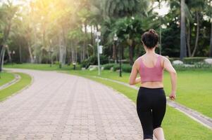 Woman jogger. back perspective portrait of young asian female wearing pink sportswear running in public park. Healthcare wellness concept. photo