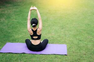 portrait fit young 30s Asian woman in pink sportswear with yoga mat. stretching muscles in park. Embrace wellness with outdoor yoga and exercise. finds balance and joy amidst nature's beauty. photo