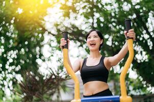 Young asian athletic sportswoman 30s wearing sportswear listening relaxing music while working out exercise equipment outdoor in park. Healthy lifestyle concept photo