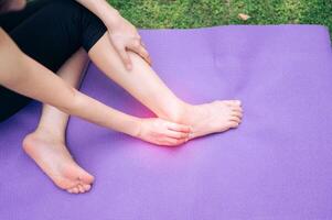 sportswoman holding her pain ankle after doing exercise on yoga mat in outdoor park. injury accident in exercise concept. photo