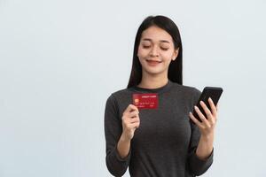 Asian woman holding showing credit card and mobile phone to shopping online isolated on white or gray background studio. Online shopping, e-commerce, internet banking, spending money concept. photo