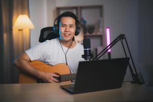 asiático hombre En Vivo transmisión actuación jugando guitarra y canta un canción. asiático hombre enseñando guitarra y canto en línea. músico grabación música con ordenador portátil y jugando acústico guitarra. foto