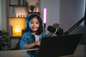 asiático joven niña sonriente En Vivo transmisión actuación jugando ukelele y canta un canción. asiático niña aprendizaje guitarra y canto en línea. músico grabación música con ordenador portátil y jugando acústico guitarra. foto