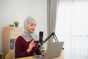 Muslim Islam freelance entrepreneur woman wearing hijab and talking while conference meeting, working using microphone and laptop and on desk table at the home office. Business conference technology. photo