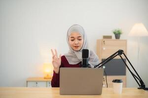 Muslim Islam freelance entrepreneur woman wearing hijab and talking while conference meeting, working using microphone and laptop and on desk table at the home office. Business conference technology. photo