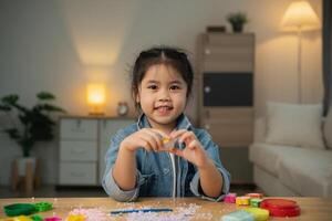 asiático linda pequeño niña aprendizaje y jugando a utilizar vistoso jugar masa en el vivo habitación a el hogar. bebé actividad educación desarrollo estilo de vida concepto. foto