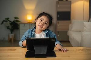 Asian child girl looking using and touch tablet display screen. Baby smiling funny time to use tablet. Too much screen time. Cute girl watching videos while tv, Internet addiction concept. photo