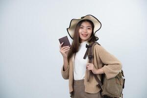 Young Asian tourist woman smiling wearing hat and holding luggage, passport and shoulder bag to prepare going to travel on holidays isolated on white or grey studio background. photo