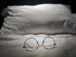 An eyeglasses optics on white linen bed, low light night time, shortsighted, nearsighted, farsighted, eyewear business products, relax or rest or sleeping time concept, focus on foreground photo
