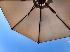Low angle view of an opened beach fabric umbrella against the blue sunny sky, view from under parasol, holiday or vacation concept, with copy space photo