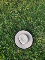 A sunhat decorated with black bow tie on lush green grass meadow, directly above view, holiday relax, picnic concept, rest time photo