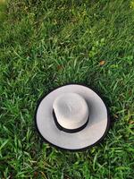 A sunhat decorated with black bow tie on lush green grass meadow, directly above view, holiday relax, picnic concept, rest time photo