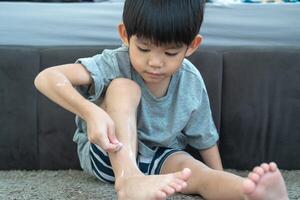 Little Asian boy's hands peeling off dry skin on his legs. Skin problems. photo