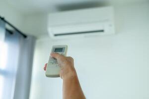 A woman's hand presses the air conditioner remote and points at the air conditioner to operate it. photo