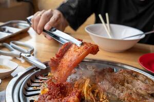 A woman's hand picks up grilled meat marinated in a Korean wok on a grill in a restaurant. photo