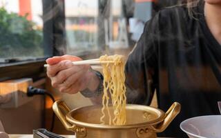 A woman's hand forks hot, smoking Korean noodles in a brass pot at a restaurant. photo