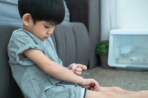 Little Asian boy's hands peeling off dry skin on his arm. Skin problems. photo