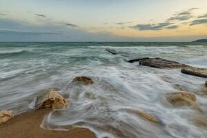 Amazing long exposure seascape with waves flowing between rocks at sunset photo