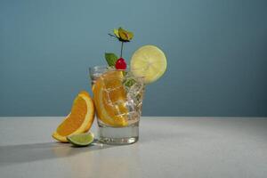 Cocktail in glass glass filled with ice and orange slice garnished with lemon slice, cherry and butterfly pin on a white table with pieces of orange and lemon photo