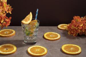 Cocktail in glass glass filled with ice and mint leaves garnished with orange slice and sorbet on a ceramic table with orange slices photo