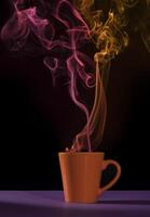 Orange cup of coffee on a purple table with red and yellow smoke photo
