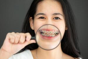 Portrait of Asian young woman in blank white t-shirt on black background with braces and magnifying glass photo