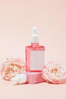 Natural organic cosmetic concept. Pink glass bottle of cosmetic product on peach background with blooming roses and copy space. Mock up of product. close up. photo