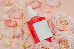 glass cosmetic bottle with a dropper on pink background with rose flowers. Natural cosmetics concept, natural essential oil and skin care products photo