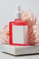 Bottle of cosmetic serum or face oil, beautiful rose flowers and petals on marble background. Skin care concept, unbranded design photo