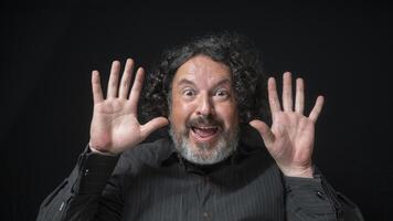 Man with white beard and black curly hair with happy and excited expression, smiling looking at camera, wearing black shirt against black background photo