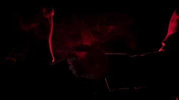 man's hand with a lit cigarette, blowing smoke, seen from profile in silhouette with red light illuminating his profile against black background photo