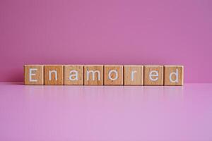 Wooden blocks form the text Enamored against a pink background. photo