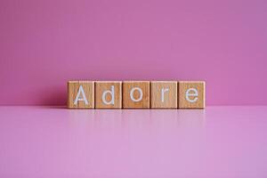 Wooden blocks form the text Adore against a pink background. photo