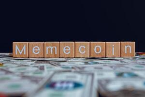 Wooden blocks with the text Memecoin on a black background and crypto banknotes scattered on the ground. photo