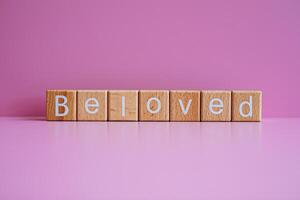 Wooden blocks form the text Beloved against a pink background. photo