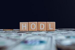 Wooden blocks with the text HODL on a black background and crypto banknotes scattered on the ground. photo