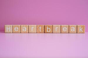 Wooden blocks form the text Heartbreak against a pink background. photo