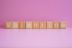 Wooden blocks form the text Valentine against a pink background. photo