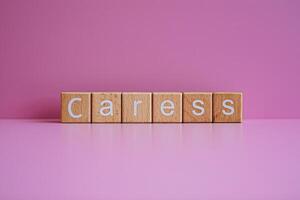 Wooden blocks form the text Caress against a pink background. photo