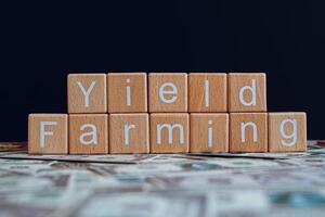 Wooden blocks with the text Yield Farming on a black background and crypto banknotes scattered on the ground. photo