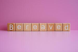 Wooden blocks form the text Bereaved against a pink background. photo