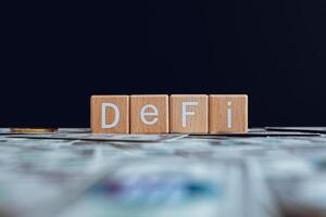 Wooden blocks with the text DeFi on a black background and crypto banknotes scattered on the ground. photo