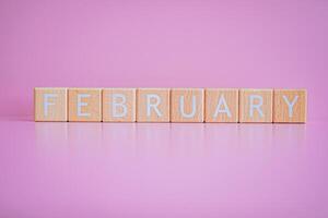 Wooden blocks form the text FEBRUARY against a pink background. photo