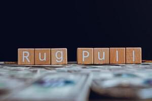 Wooden blocks with the text Rug Pull on a black background and crypto banknotes scattered on the ground. photo