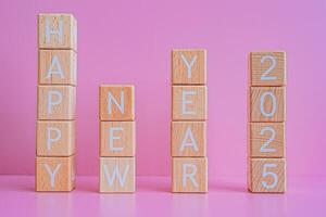 Wooden blocks form the text HAPPY NEW YEAR 2025 against a pink background. photo